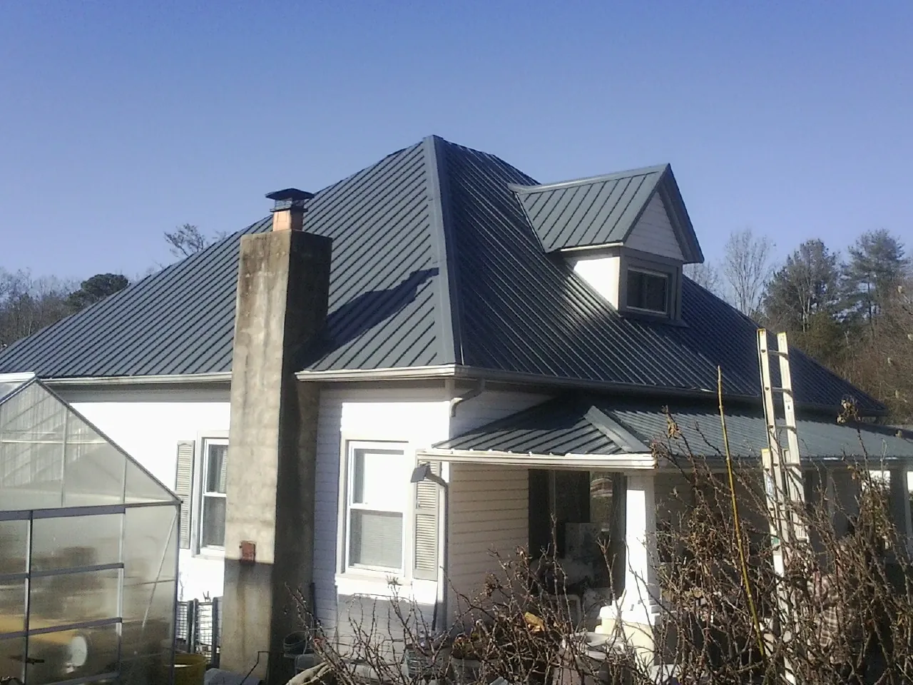 Dark blue standing seam metal roof on a white farmhouse with dormer — Slate & Tile Roof Repair by Roofing Brothers in Bergholz