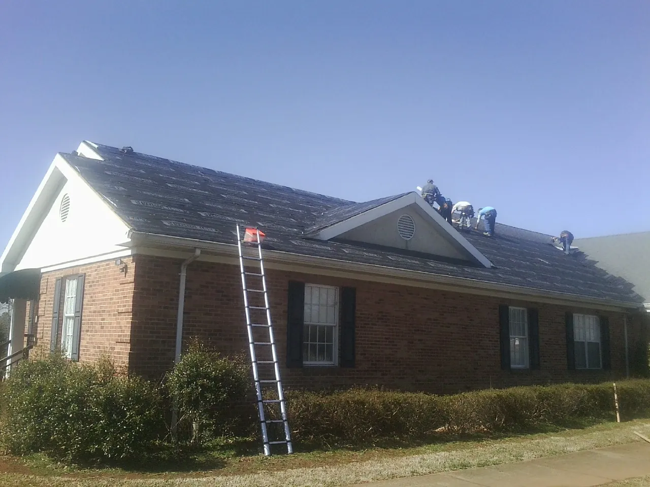 Crew tearing shingles off a brick ranch roof with a ladder set — Emergency Roof Repair work by our crew in Bergholz