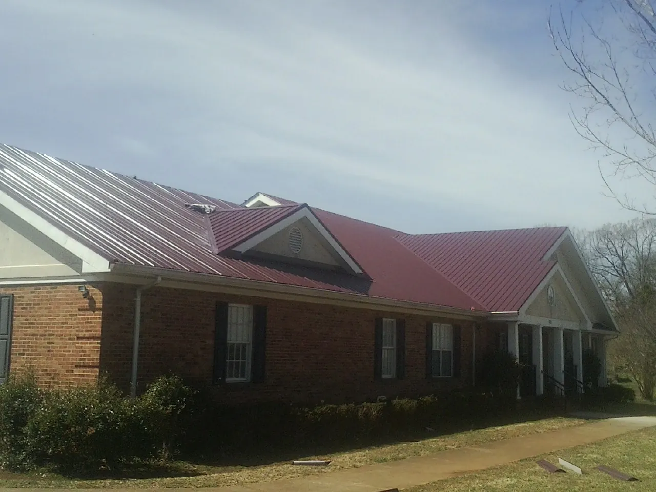 Red metal roof with gabled entries on a long brick building, from a Hail Damage Roof Repair job in Bergholz