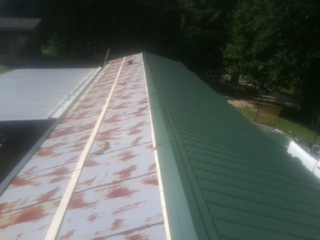 Old rusted panels beside newly installed green metal roofing — Wind Damage Roof Repair by Roofing Brothers in Bergholz
