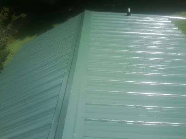 New green metal panels meeting at the ridge of a roof — Flat Roof Repair work by our crew in Bergholz