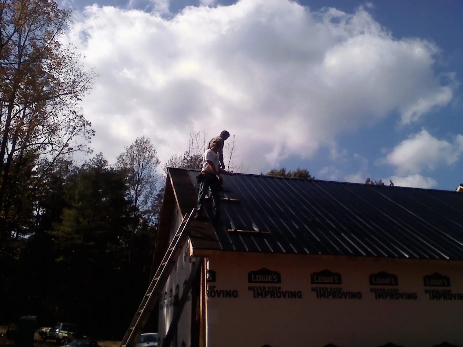 Roofer fastening dark metal panels high against a cloudy sky, from a Roof Inspection job in Bergholz