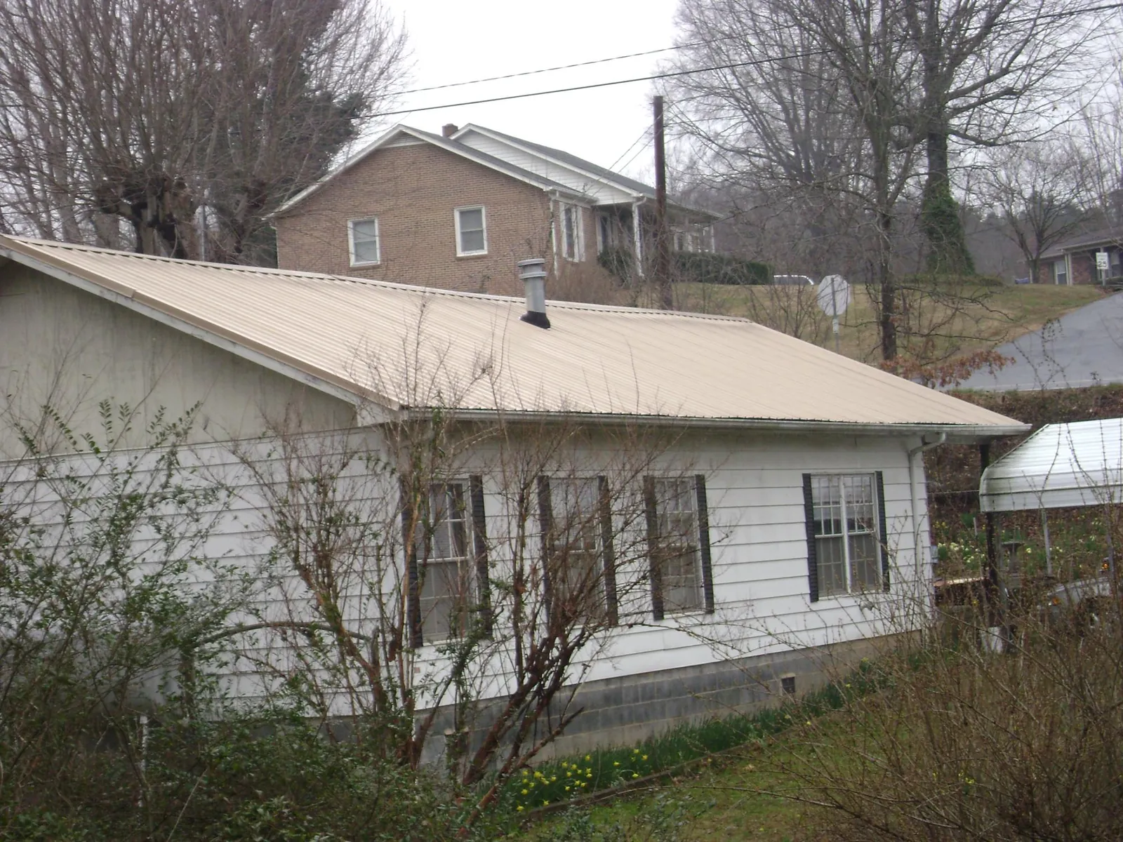 Tan metal roof on a white sided house set into a hillside — Commercial Roofing by Roofing Brothers in Bergholz