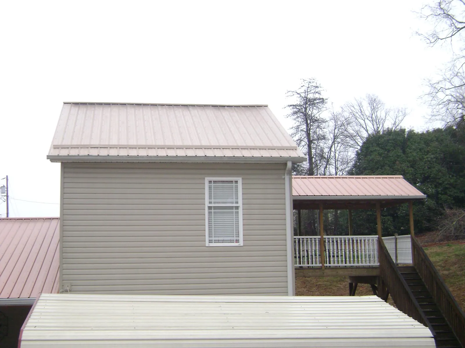 Tan metal roofs on a two story addition and attached porch, from a Roof Replacement job in Bergholz